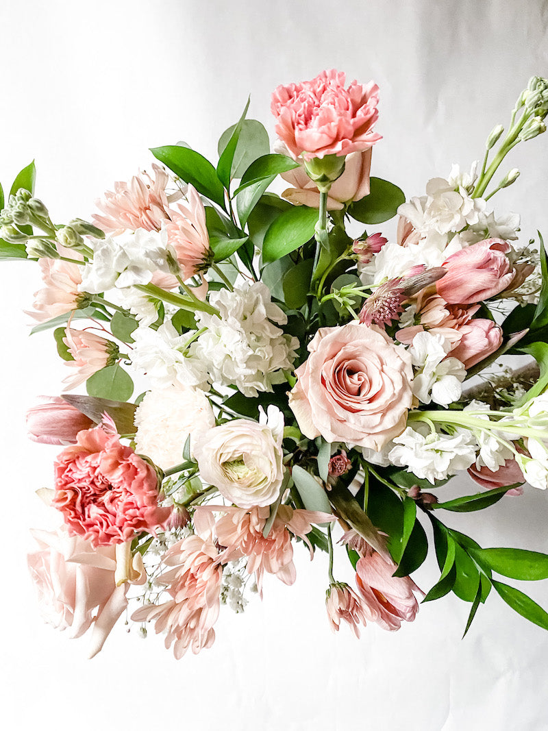 Whimsical hand-tied bouquet of seasonal flowers in shades of pink and ivory with greenery