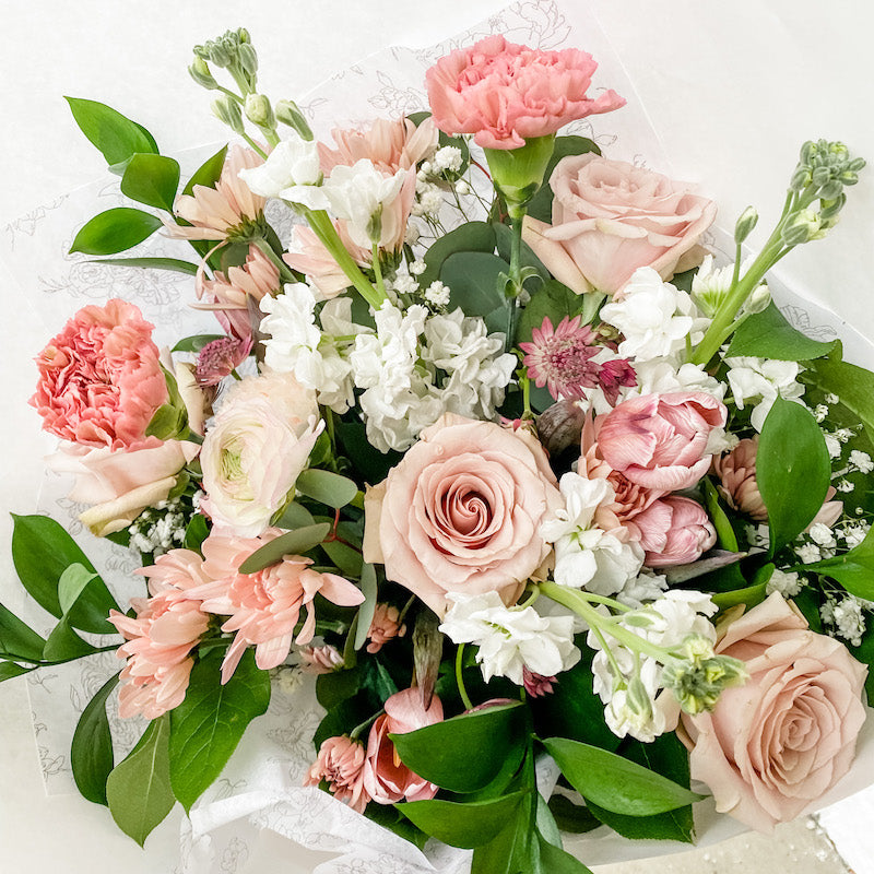 Whimsical hand-tied bouquet of seasonal flowers in shades of pink and ivory with greenery